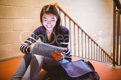 Smiling student sitting in hallway using laptop