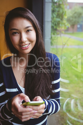 Smiling student leaning against the glass window using smartphon
