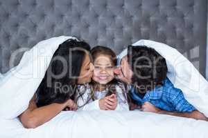 Happy parents kissing daughter