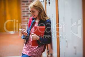 Smiling student leaning against the locker using smartphone