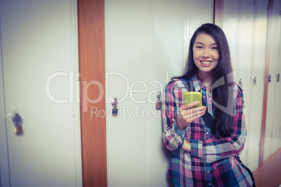 Cheerful student standing next the locker and using smartphone