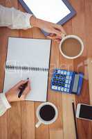 Cropped image of woman with coffee cup writing on notepad