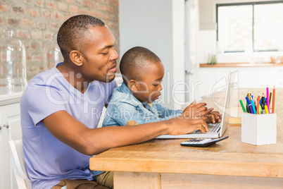 Cute son using laptop at desk with father