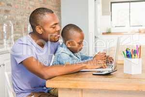 Cute son using laptop at desk with father