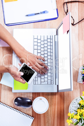 Overhead of feminine hands using laptop and smartphone