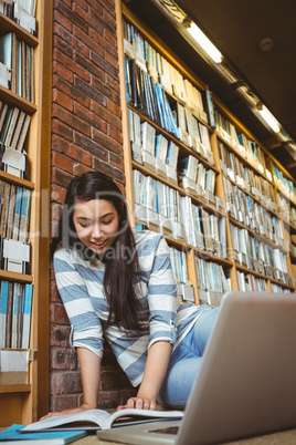 Smiling student sitting on the floor against wall in library stu