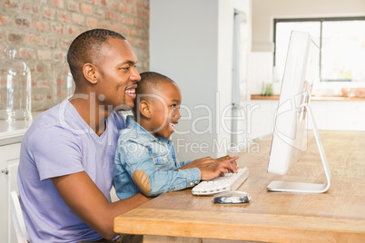 Cute son using laptop at desk with father