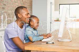 Cute son using laptop at desk with father