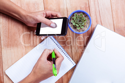 Feminine hands holding smartphone and taking notes