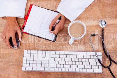 Doctor using mouse and writing on diary