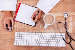 Doctor using mouse and writing on diary