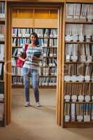 Pretty student standing in library holding a book