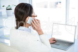 Rear view of businesswoman on phone using laptop