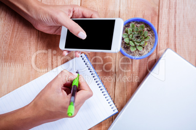 Feminine hands holding smartphone and taking notes