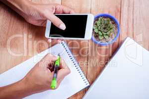 Feminine hands holding smartphone and taking notes