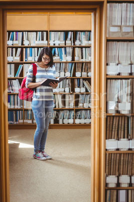 Pretty student with backpack reading a book in library