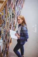 Standing student reading book in library