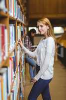 Blond student looking for book in library shelves