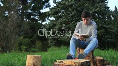 Young man sitting in a park and reading a book
