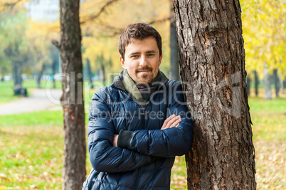 Handsome guy leaned against a tree in autumn park