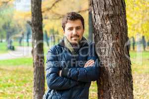 Handsome guy leaned against a tree in autumn park