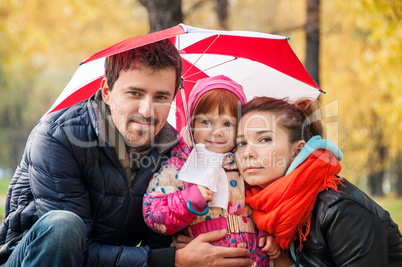 Happy young family under an umbrella in an autumn park