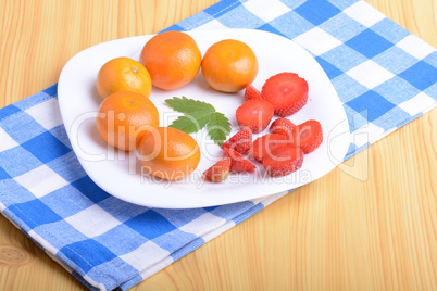 A slice of red strawberry on white plate with mandarin and strawberry slices