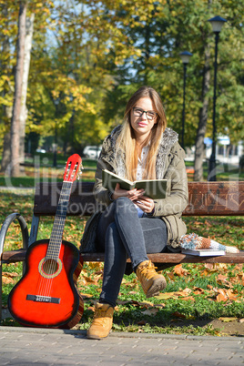 Girl, book and guitar on a bench