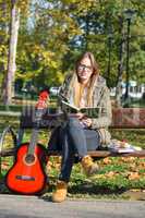 Girl, book and guitar on a bench