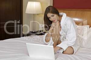 Laughing woman using a laptop sitting on bed