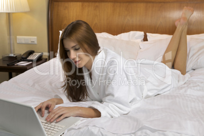woman looking at a laptop lying on bed at home