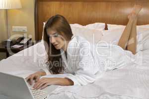 woman looking at a laptop lying on bed at home