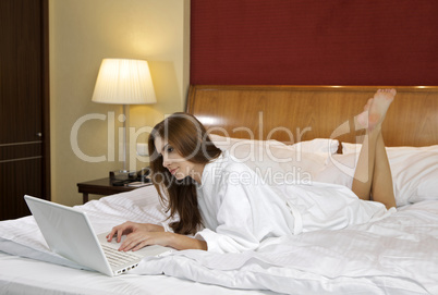 Brunette woman looking at a laptop lying on bed at home