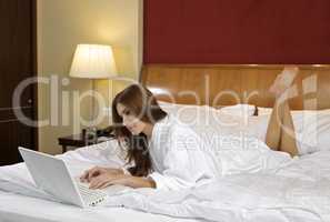 Brunette woman looking at a laptop lying on bed at home