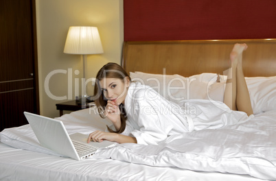 young woman lying on a white sofa with a laptop.