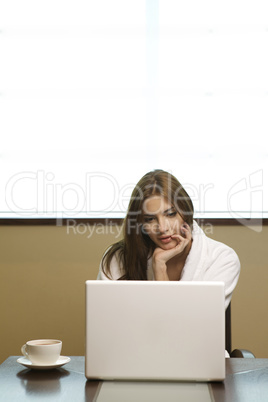 Young woman looks at her laptop computer and drinks her coffee