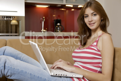 young woman lying on a white sofa with a laptop.