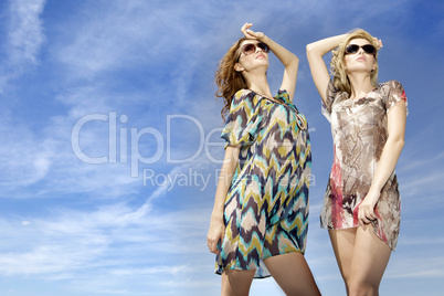 two beautiful girl in sunglasses on background blue sky