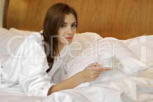 Portrait of beautiful woman with cup on bed