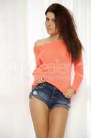 Young slim sexy woman in orange sweater against the window
