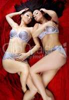 two sexy beautiful brunette girls lying on red background bright