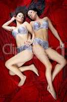 two sexy beautiful brunette girls lying on red background bright