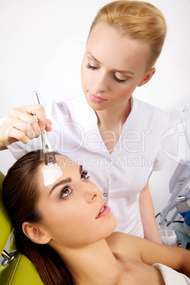 young woman getting beauty skin mask treatment on her face with