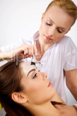 young woman getting beauty skin mask treatment on her face with