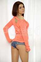 Young slim sexy woman in orange sweater against the window