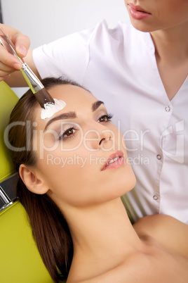 young woman getting beauty skin mask treatment on her face with