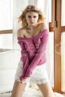 Young slim sexy woman in pink sweater against the window