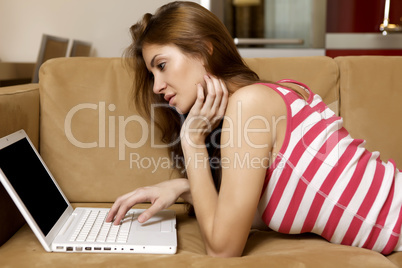 young woman lying on a white sofa with a laptop.