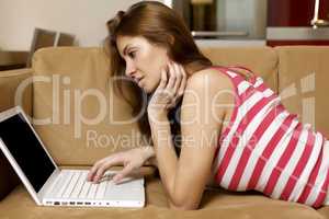 young woman lying on a white sofa with a laptop.