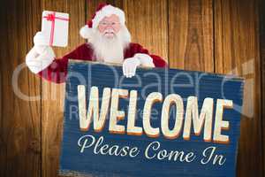 Composite image of santa shows a present while holding sign